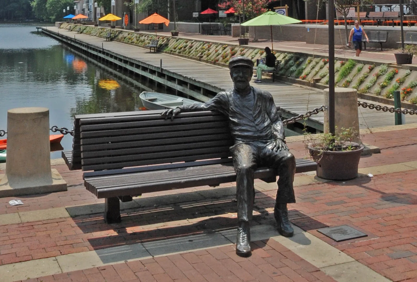 A bronze statue of Reston founder Robert E. Simon sits on a bench beside the boardwalk at Lake Anne Plaza.